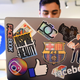 a man on a laptop with several stickers with Facebook and Instagram logos on it sits next to a giant sign with the Facebook thumb up